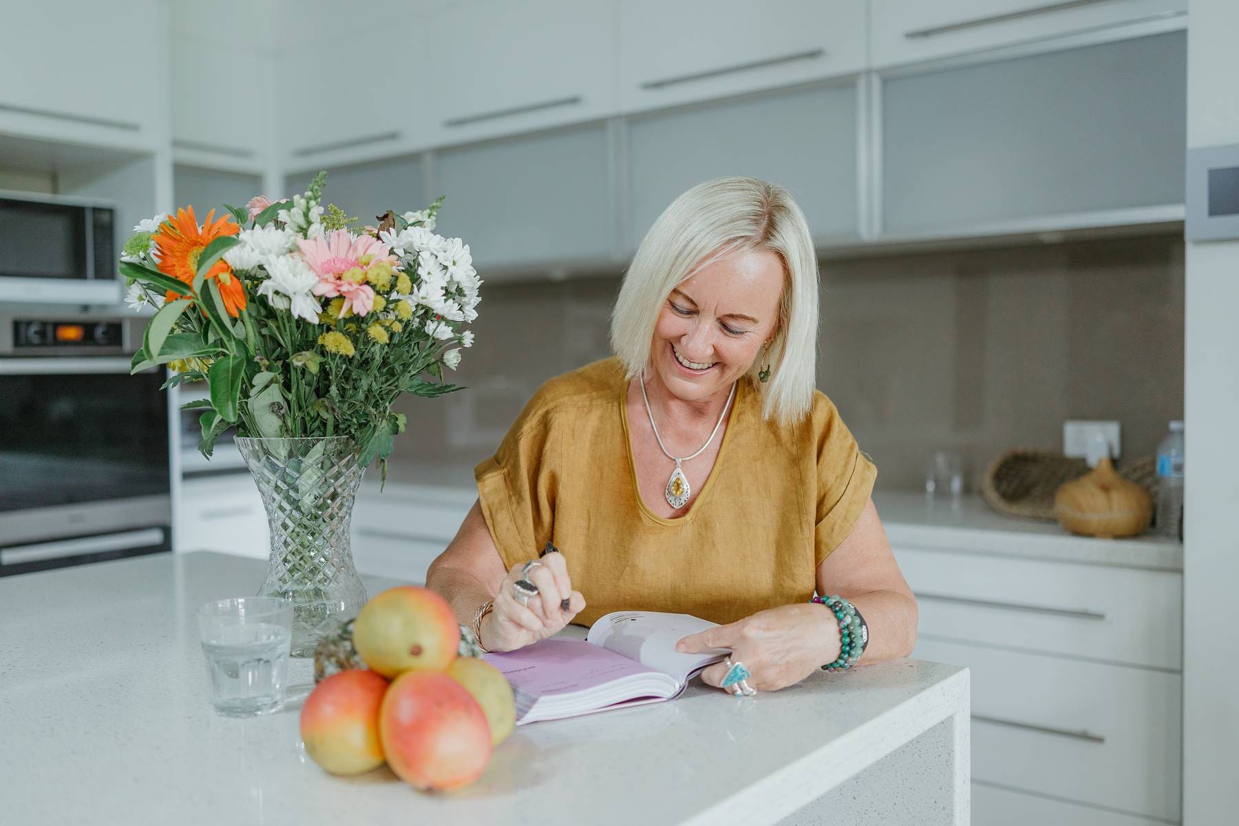 Kathy Morrison Simple Wellness and Lifestyle Habits Kathy Morrison writing in journal at kitchen bench, supporting simple wellness and lifestyle habits for women over 40